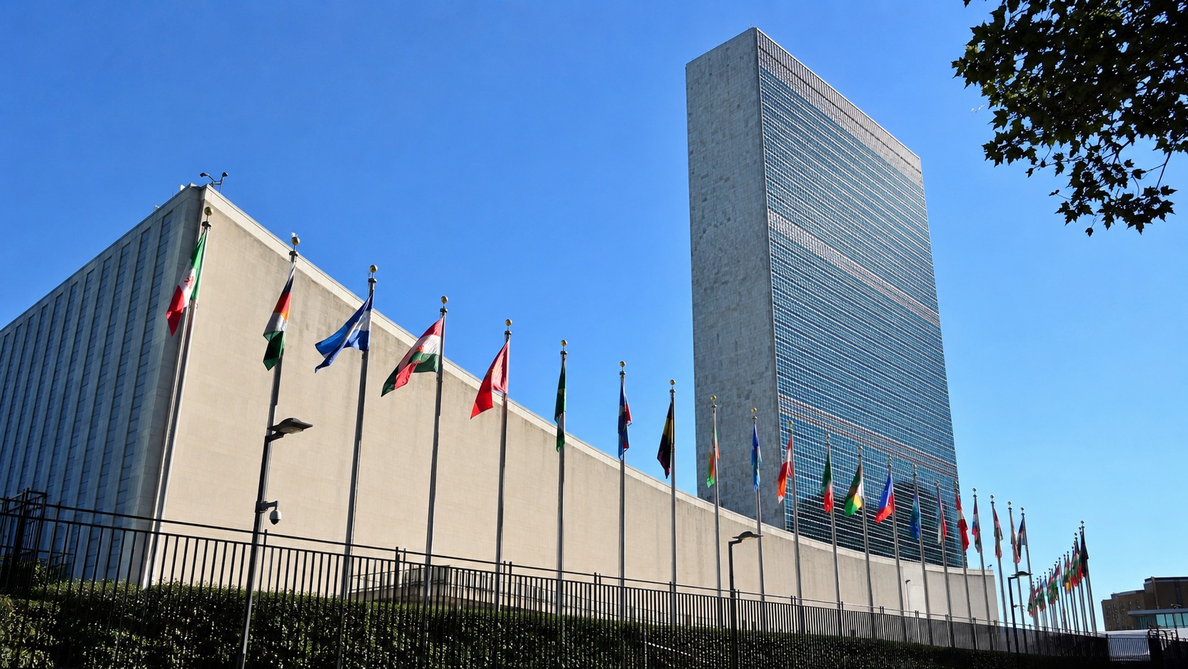 Siège de l’ONU à New York, bâtiment des Nations Unies avec drapeaux internationaux, ciel bleu ensoleillé, 30 juin 2026, format 16/9