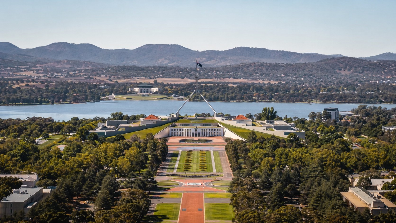Photo professionnelle ultra réaliste format 16/9 de Canberra capitale de l’Australie avec vue panoramique sur le Parlement australien, le lac Burley Griffin, les jardins arborés et les collines en arrière-plan sous une météo ensoleillée.